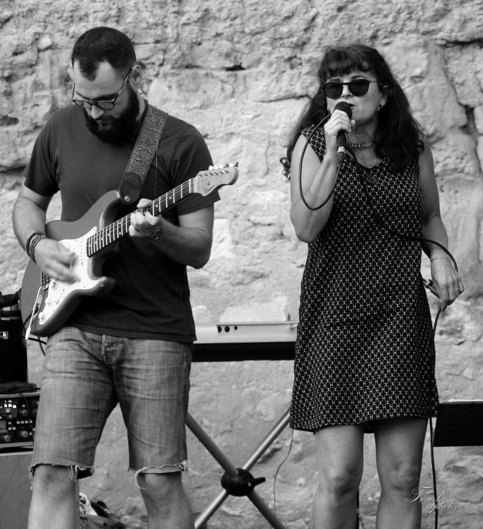 une photo en noir et blanc de Vince concentré sur sa guitare et Véro au chant dans sa robe à pois